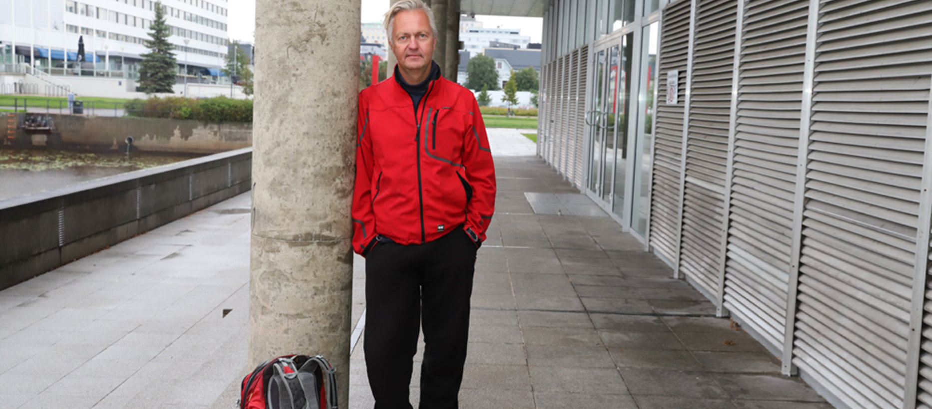 Kuvassa Markku Heikkinen seisoo kirjaston takana ja nojaa pylvääseen.
