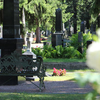 Kuvassa on näkymä Oulun hautausmaalta, hautakiviä ja takorautainen penkki.