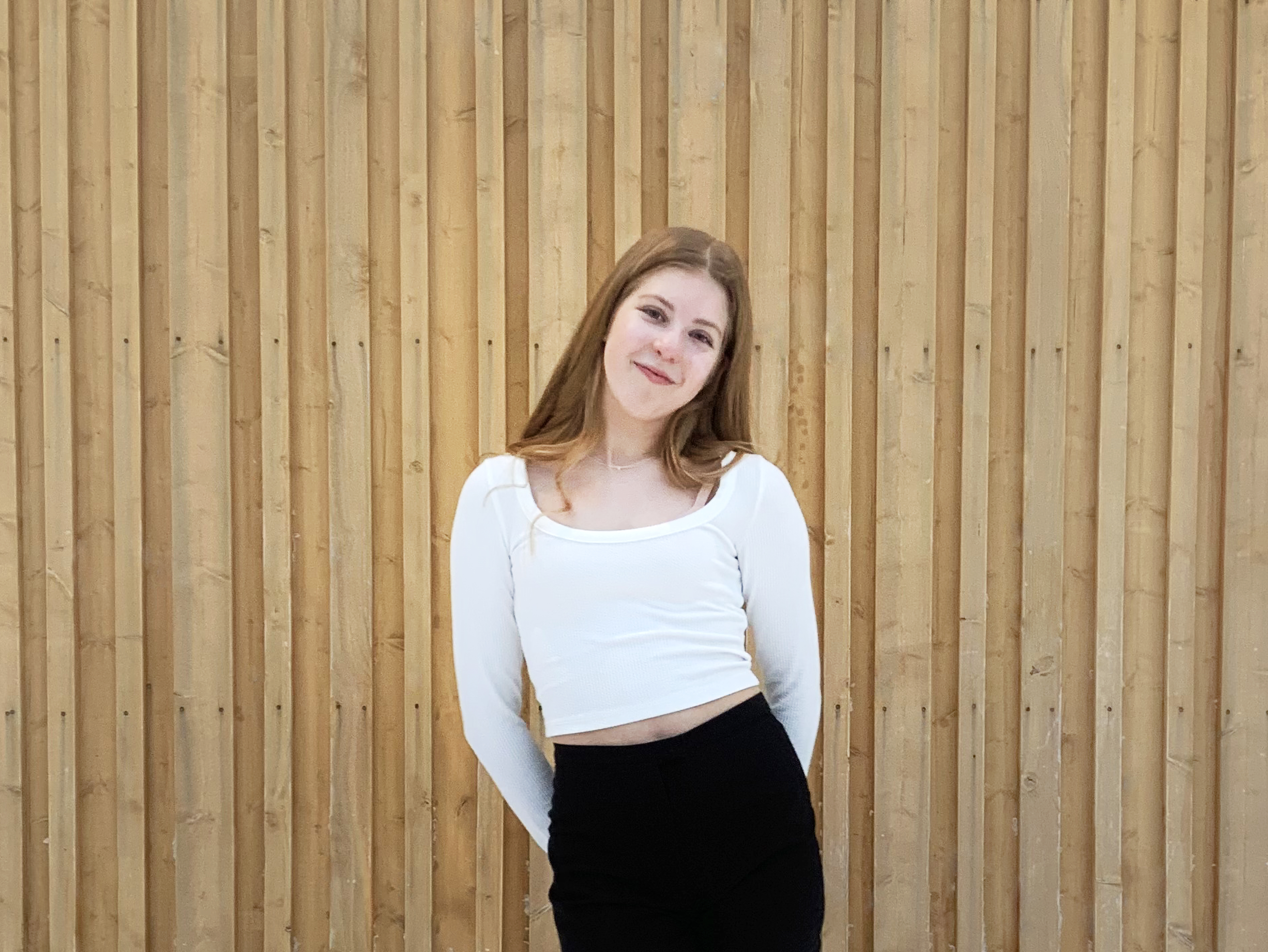 Ellen Toikkanen seisoo Hiukkavaaran monitoimitalon edessä, hymyilee ja katsoo kameraan.