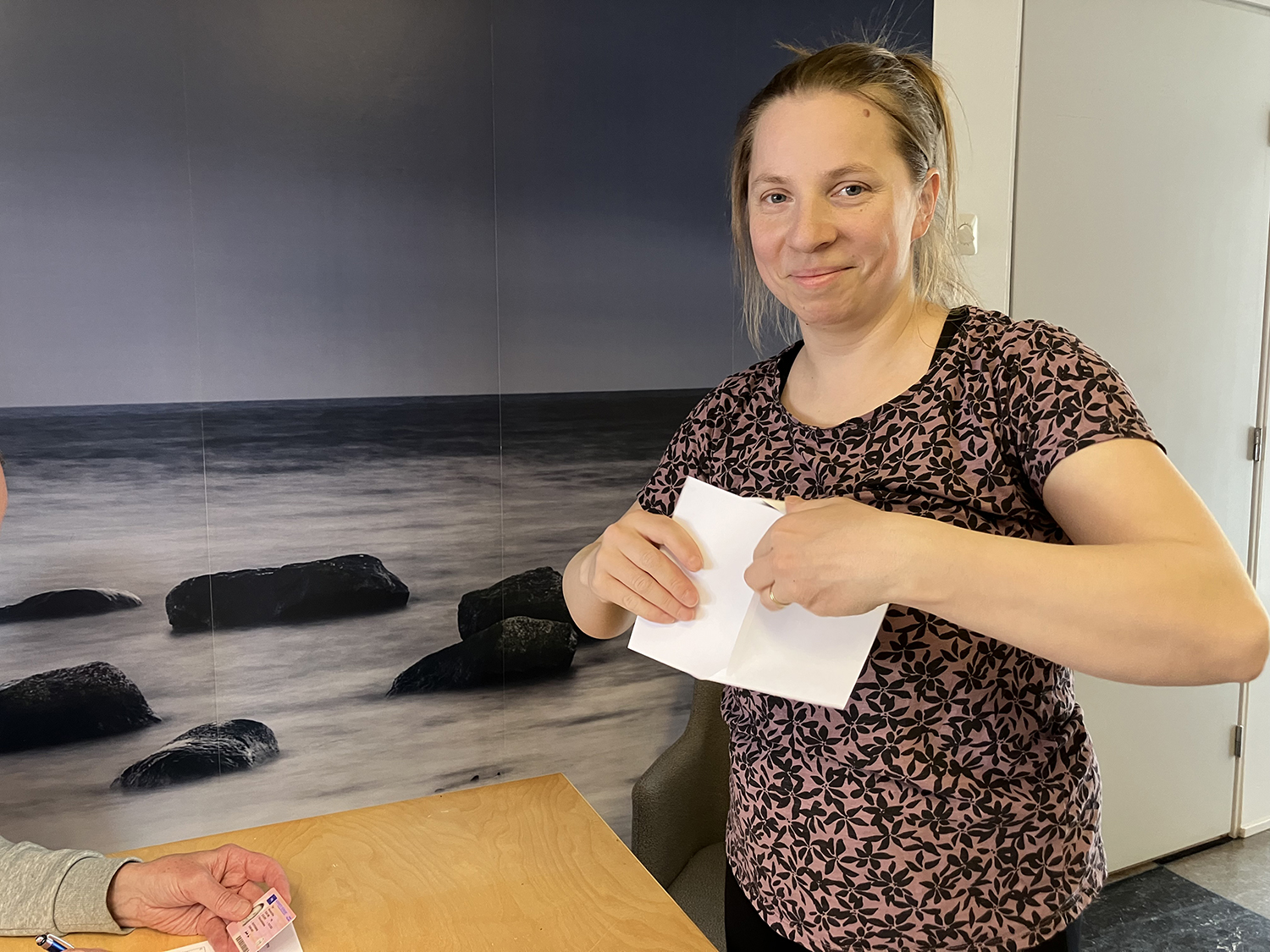 Henkilö pitää käsissään äänestyslipuketta ja katsoo kameraan hymyillen.