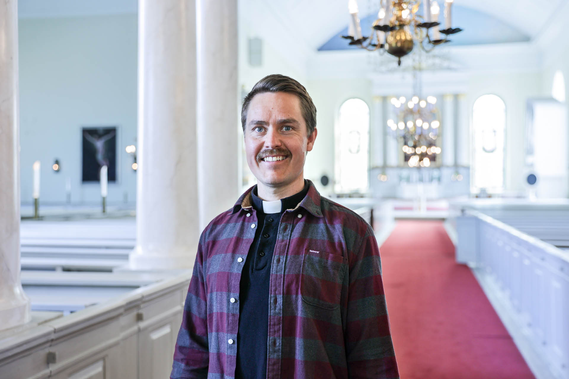 Hymyilevä pastori Lauri Holma Oulun tuomiokirkon kirkkosalissa.