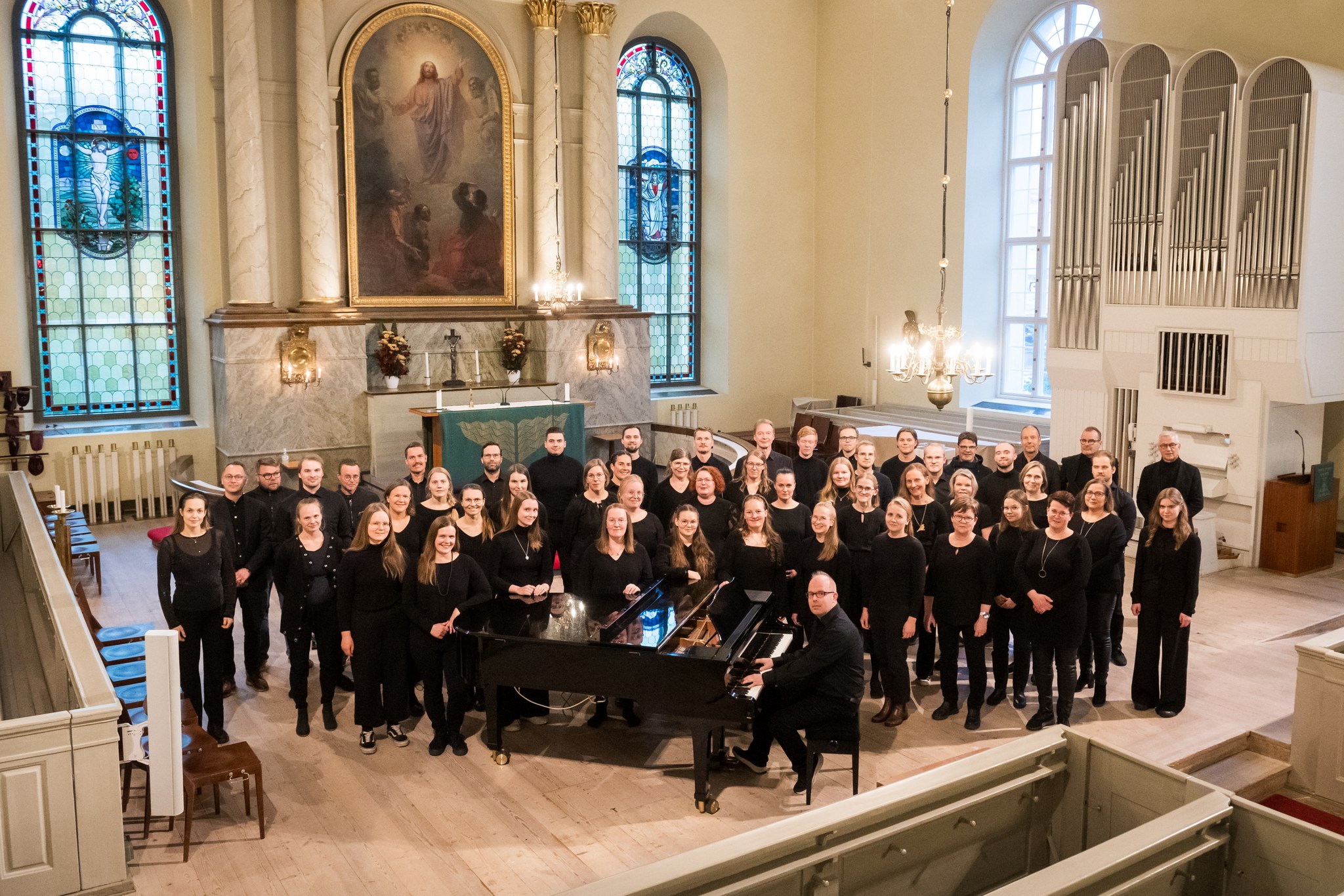 Kuoro, jossa on monta kymmentä jäsentä, seisoo tuomiokirkon alttarilla Lauri-Kalle Kallungin istuessa piano...