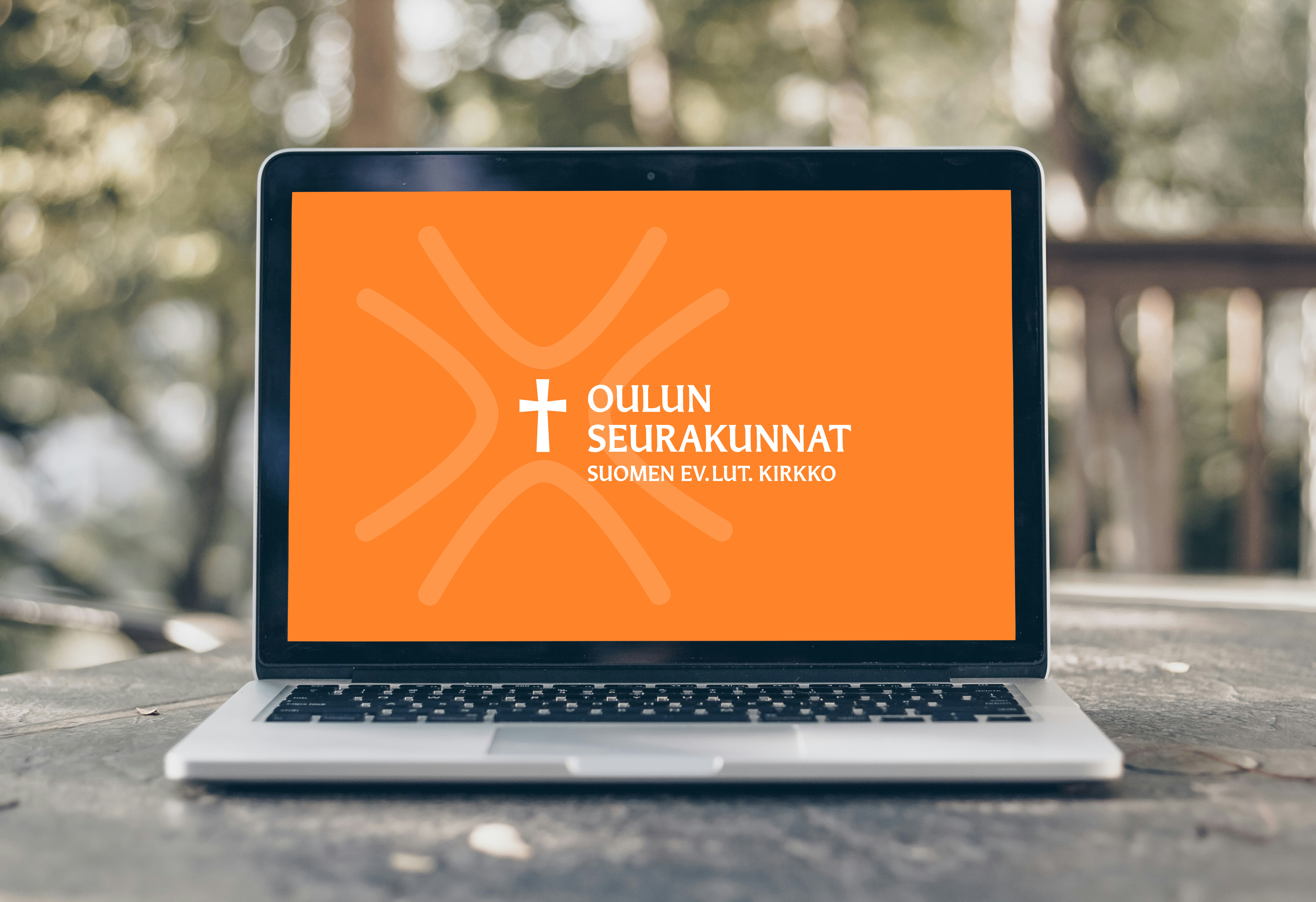 Oulun seurakuntien uusi logo oranssilla pohjalla kannettavan tietokoneen näytöllä.