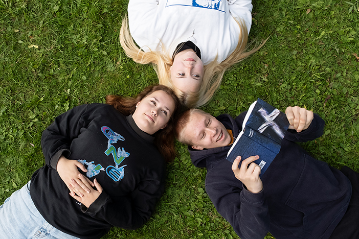 Kolme rippikoululaista makaa maassa ja yksi lukee raamattua