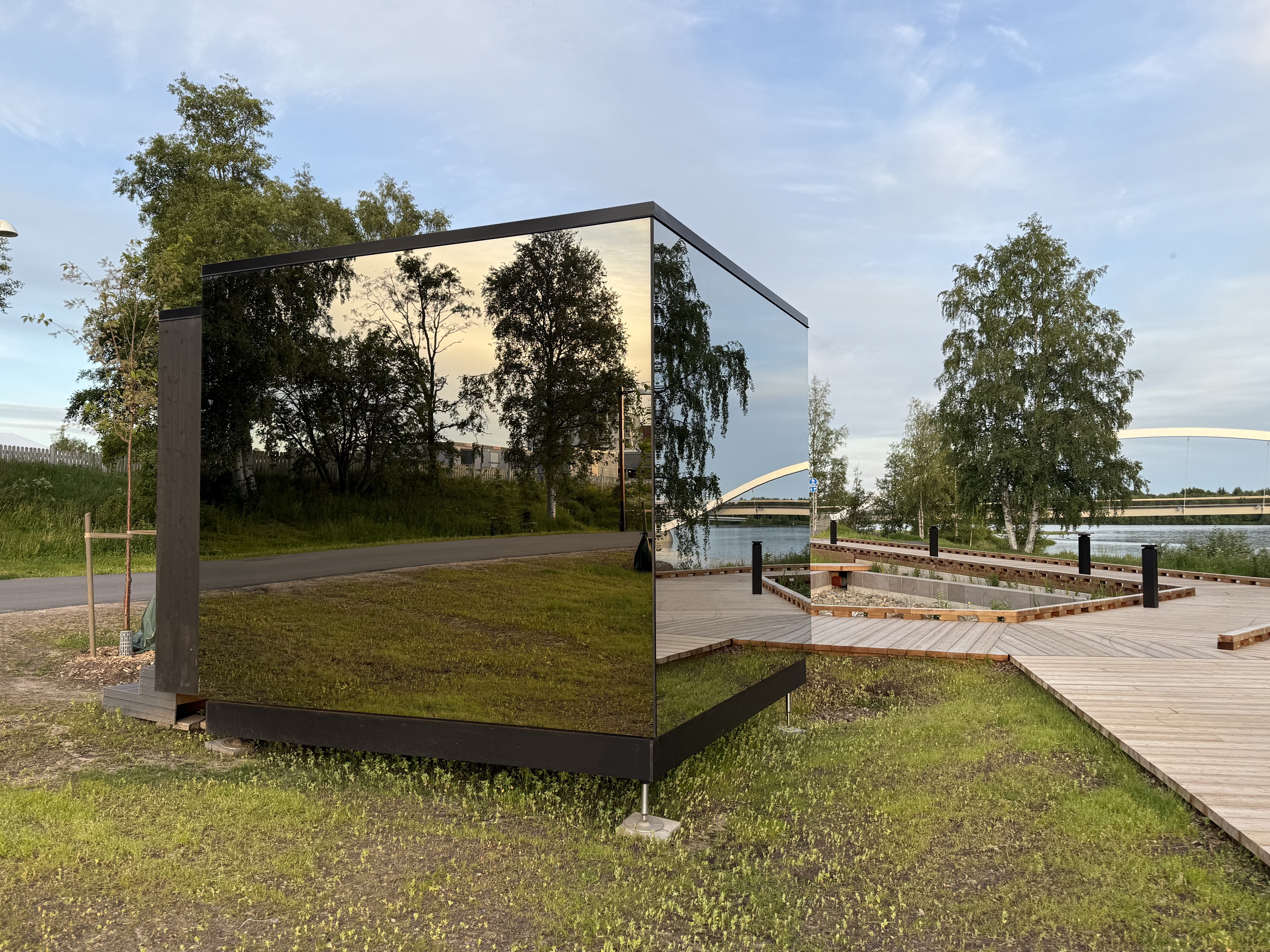 Kuution näköinen rakennus, jonka seinät ovat peililasia ja joista heijastuu rakennuksen ympärillä oleva luo...