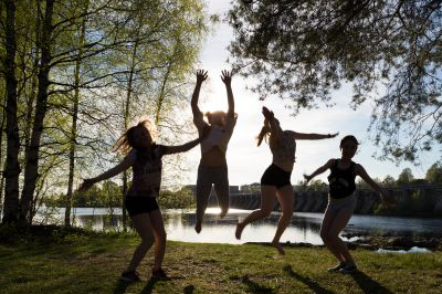Nuoret hyppivät iloisina Ainolan puistossa aurinkoisena kesäpäivänä.