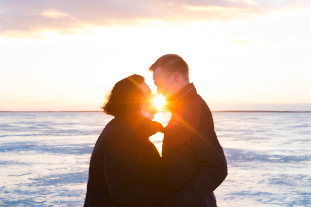 Kuvassa pariskunta lumella auringonlaskun edessä.