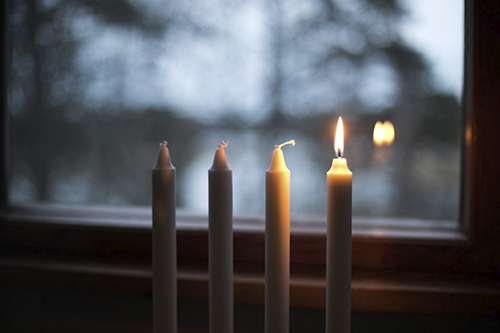 Neljä valkoista kynttilää ikkunalla, yksi kynttilä on sytytetty