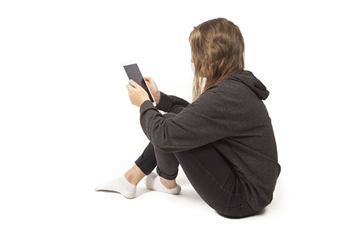 Nuori tyttö istuu lattialla kännykkä kädessä
