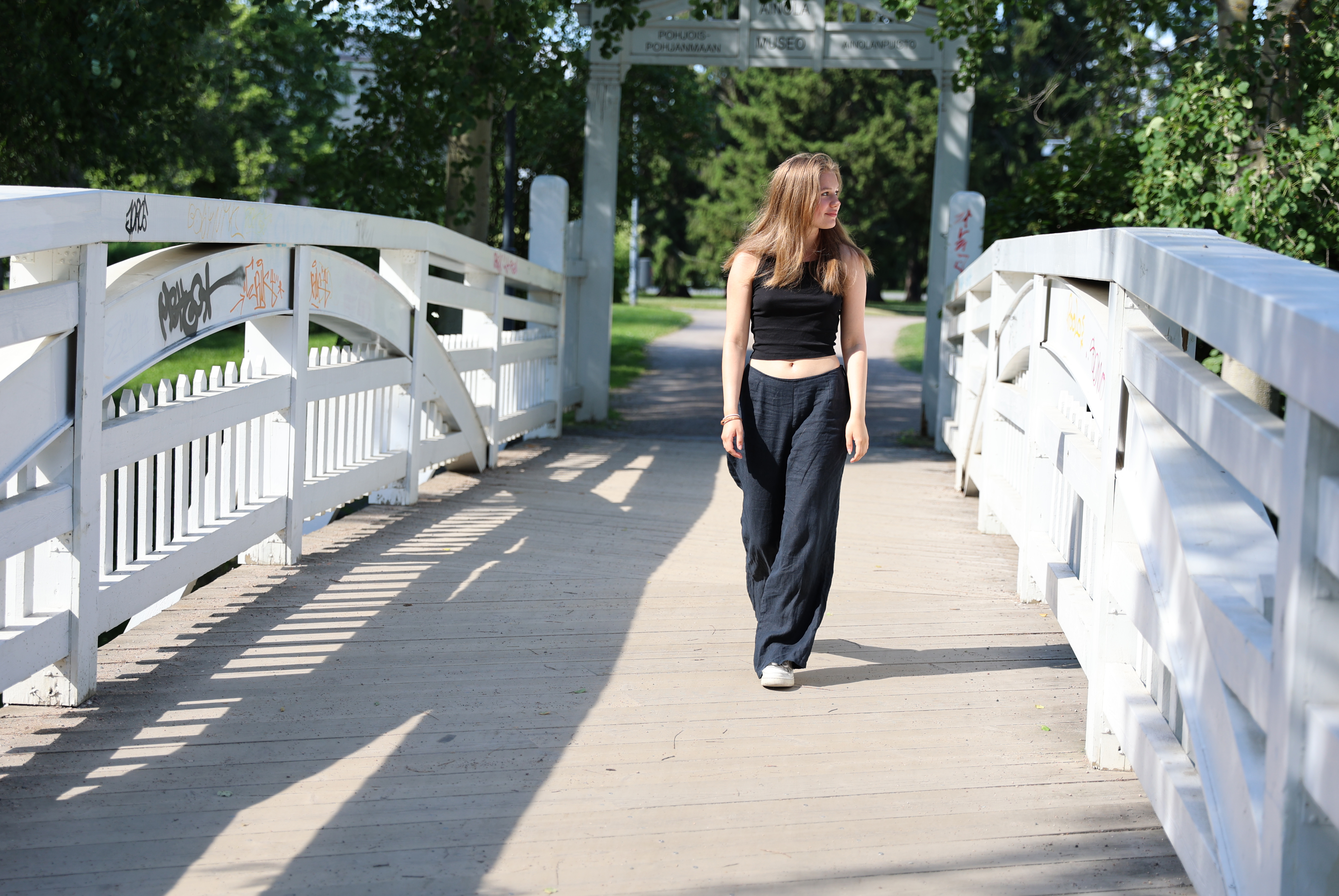 Nuori nainen kävelee siltaa pitkin Ainolan puistossa kesällä.