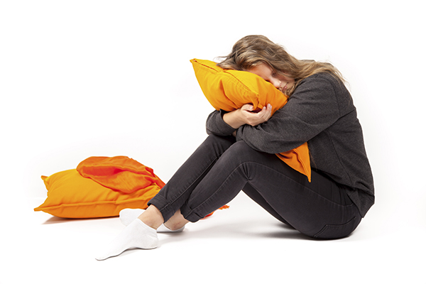 Tyttö istuu lattialla ja puristaa oranssia tyynyä sylissään kasvot tyynyyn päin.
