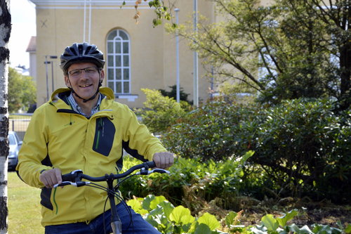 Piispa Jukka Keskitalo pyöräilemässä Oulun tuomiokirkon luona.