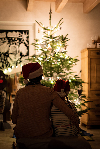 Joulukuusen edessä vanhempi ja lapsi vierekkäin, selin kameraan