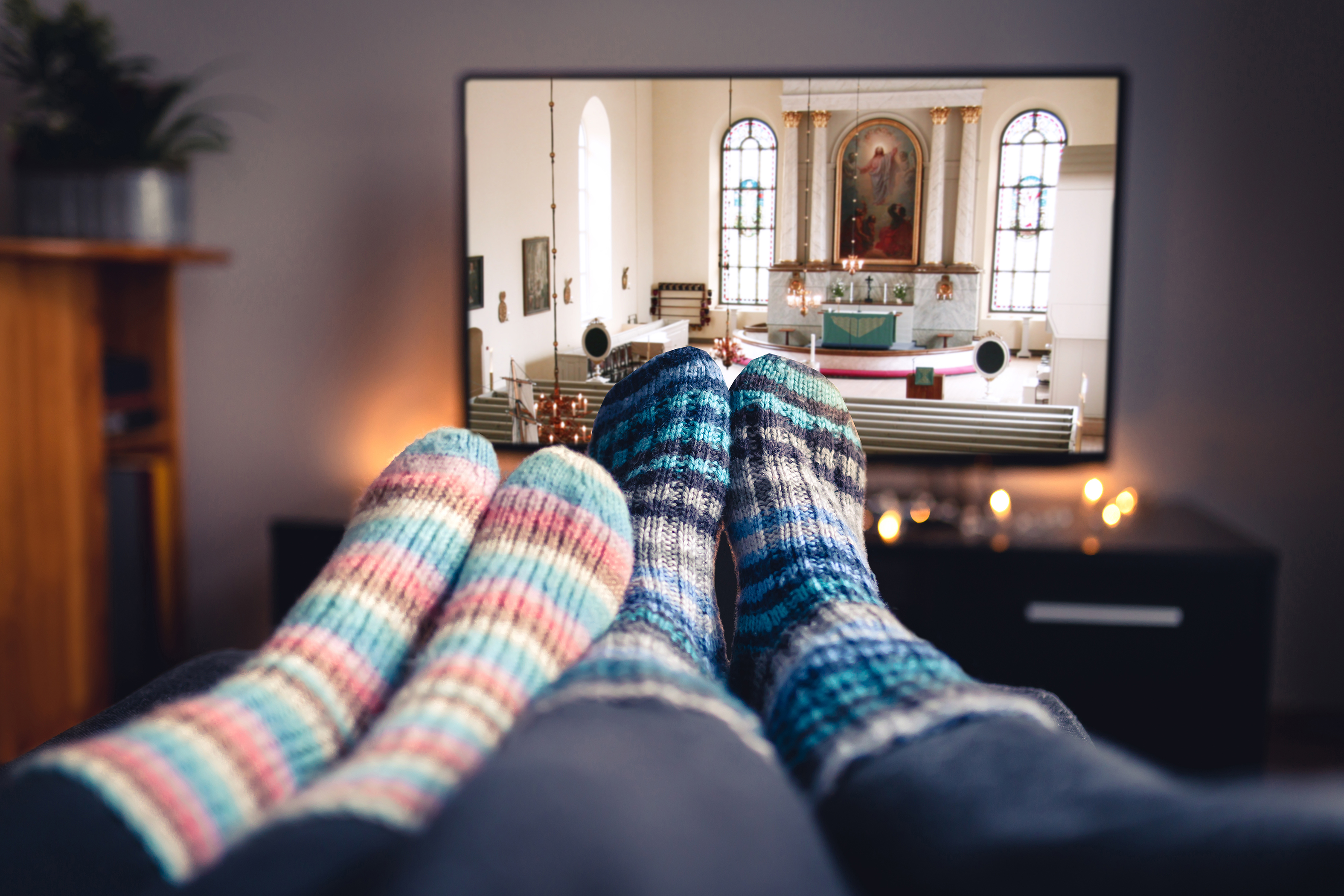 Ihmiset villasukkineen katsovat Virtuaalikirkkoa kotisohvalta. Kuva: Shutterstock  