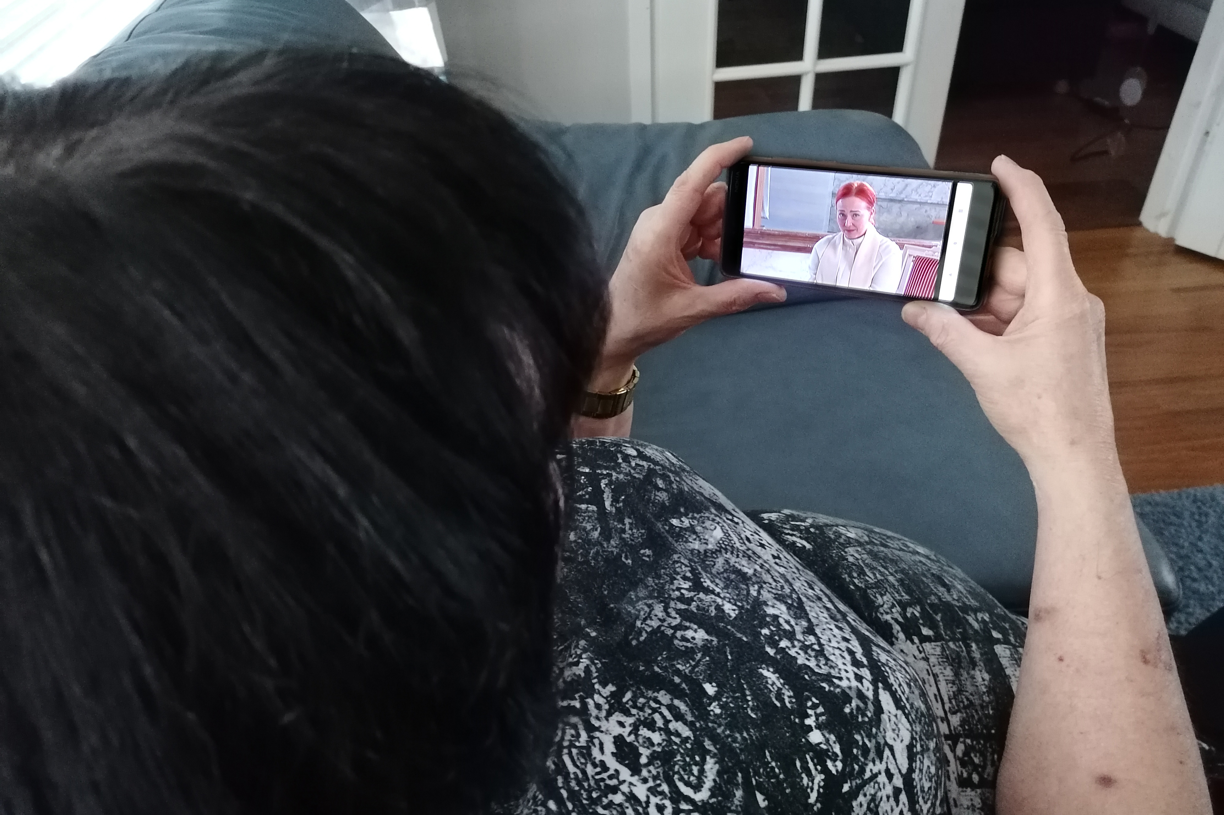 Kuvassa nainen katsoo matkapuhelimesta virtuaalikirkon lähetystä