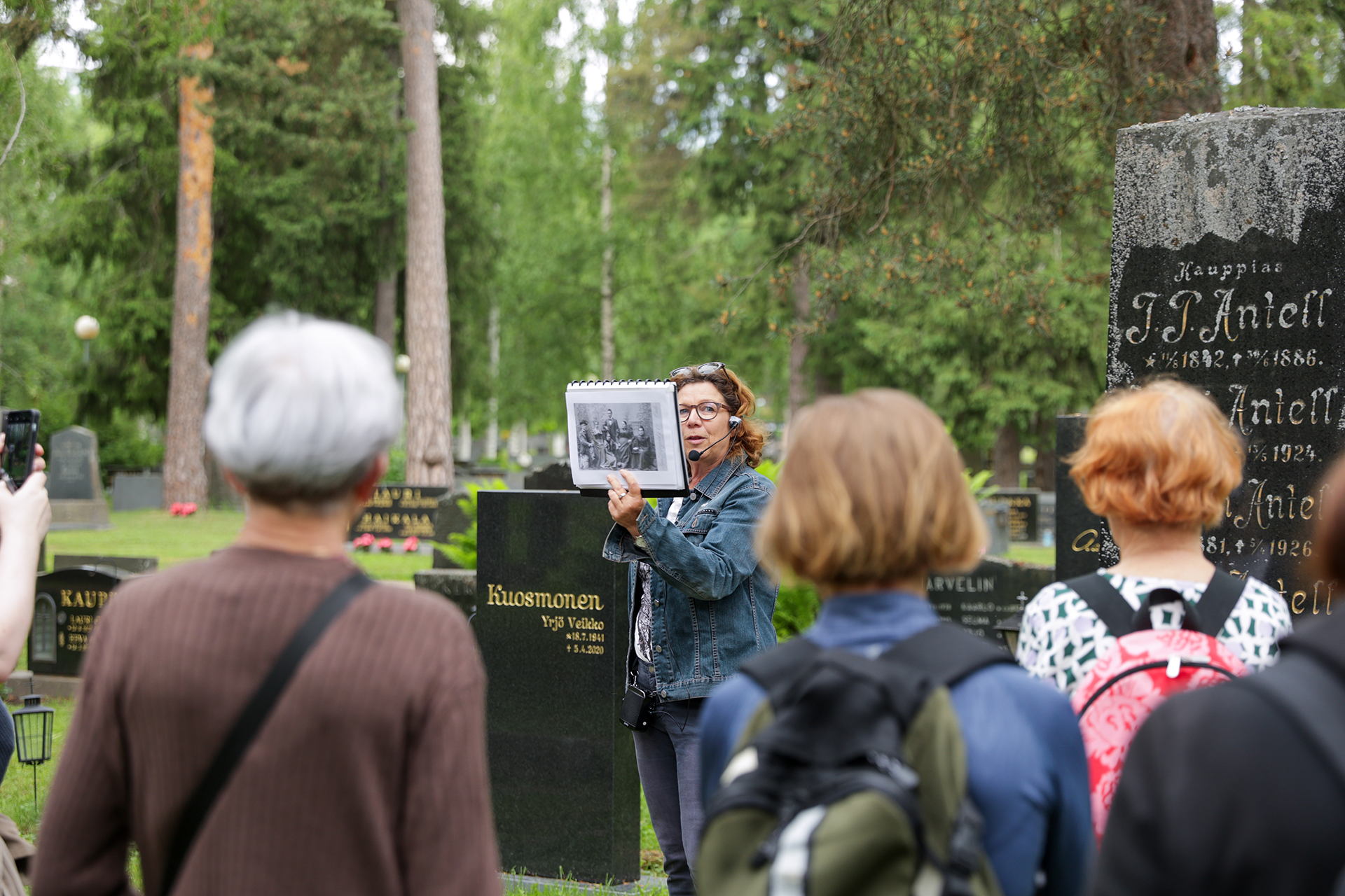 Opas puhumassa hautausmaakierroksella, kuulijoita selin kameraan.