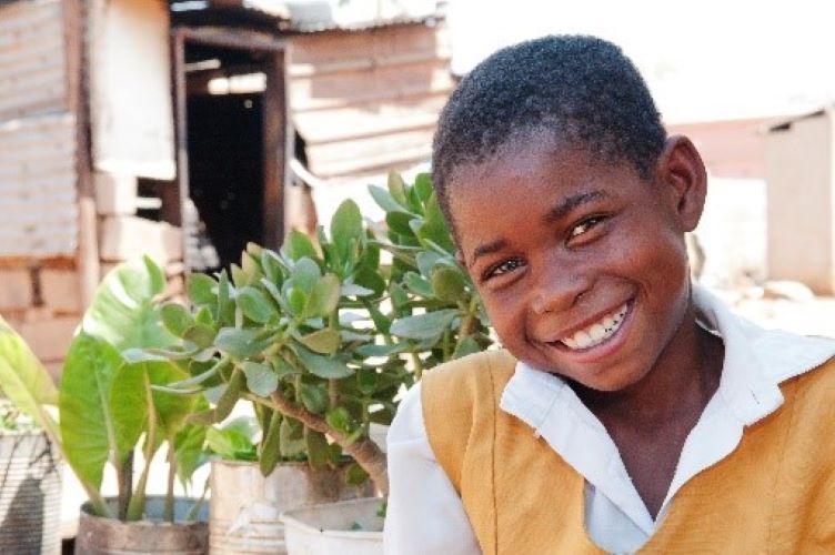 Botswanalainen koululainen hymyilee kelta-valkoisessa koulupuvussaan taustallaan viherkasveja