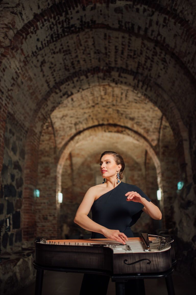Ida Elinan konsertti Kuvaaja V-P Kangas, Kuvassa Ida Elina tummassa juhlamekossa sekä kantele. Taustalla holvikaaret.