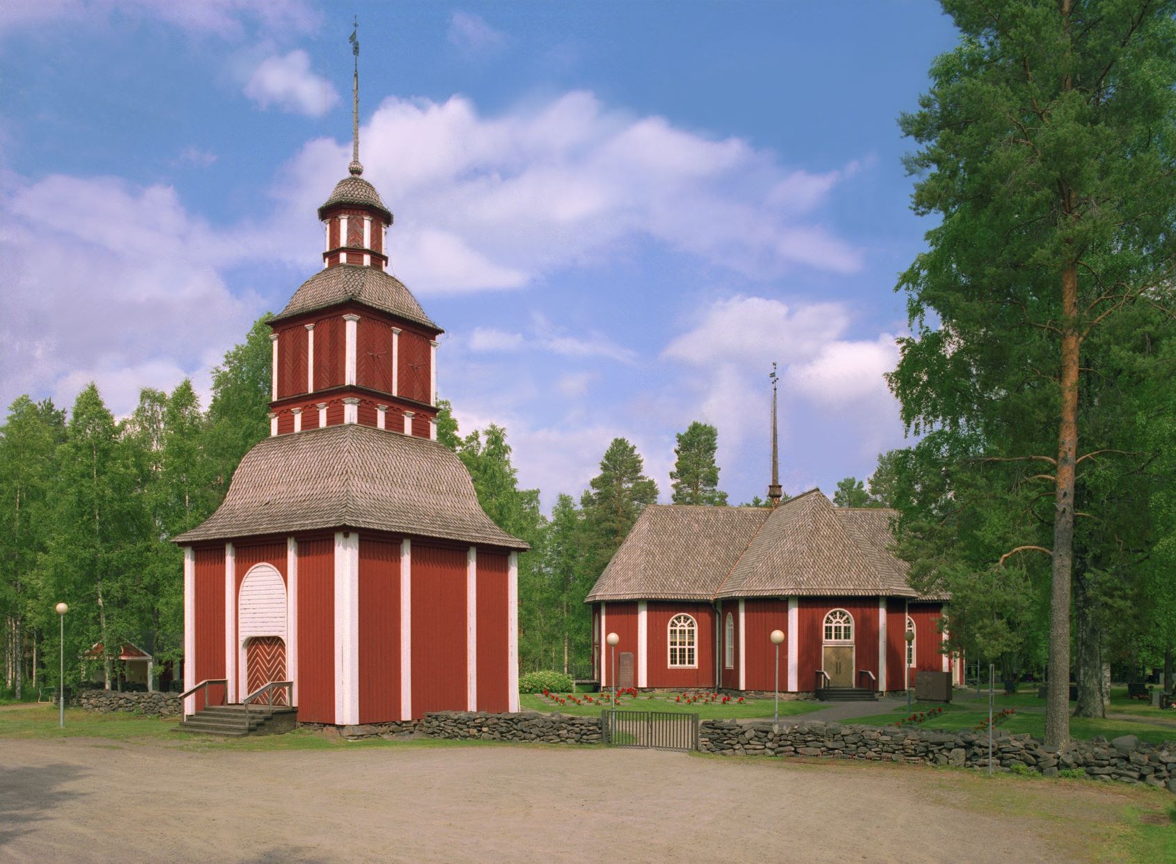 Edustalla punainen Kiimingin kirkon tapuli, taustalla Kiimingin kirkko ja kesäisen vihreitä puita