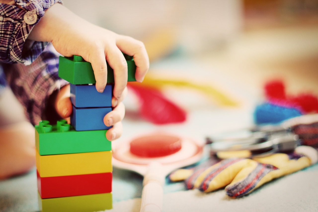 Kuvassa lapsen kädet, legopalikat ja taustalla muita leluja