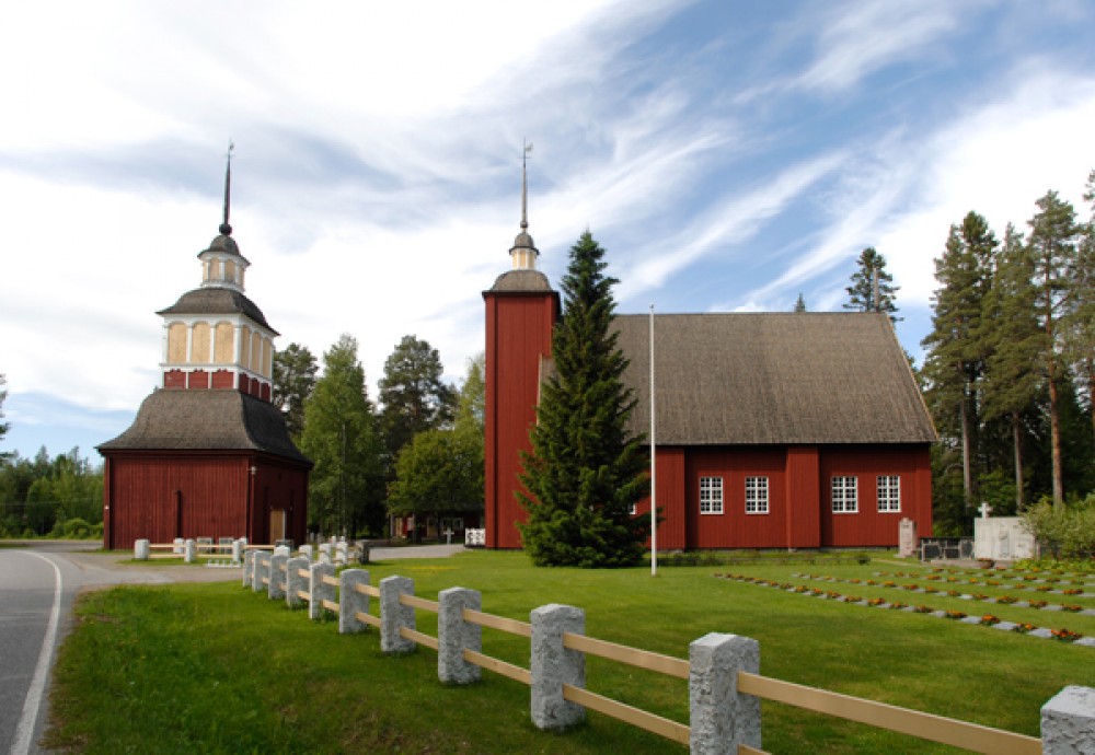 ​​Utajärvi Church from the outside. Red, wooden church, pictured on a sunny day. 