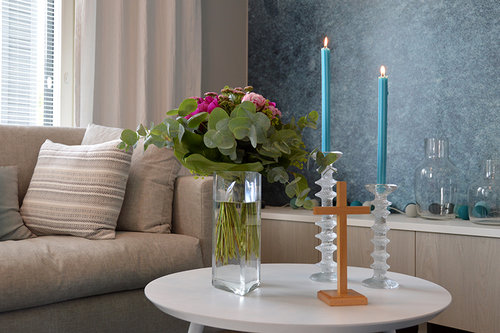 Näkymä olohuoneesta kodin siunausta varten. Sohvapöydällä kynttilät, risti ja kukat.