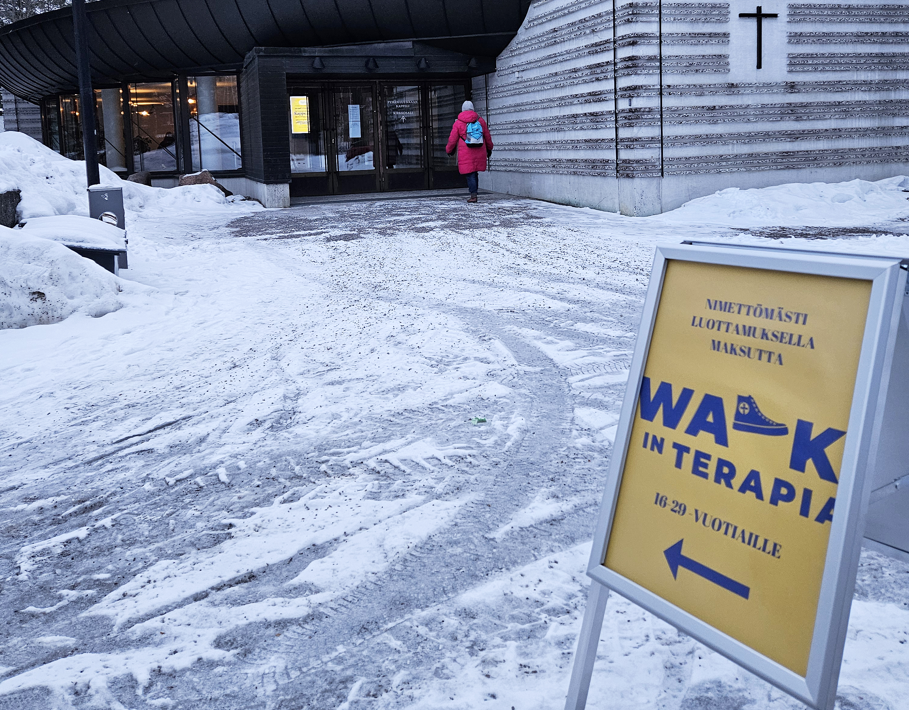 Ihminen kävelee Pyhän Luukkaan kappeliin, kuvan etualalla on kyltti, jossa lukee walk in terapia.